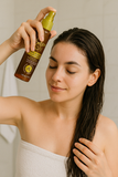 Woman applying Argan Oil Heat Defence Leave-In Spray to wet hair for protection and hydration before heat styling.